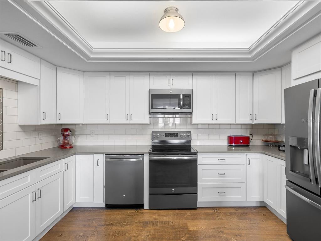 A kitchen with white cabinets, dark stainless steel appliances, and wood-look flooring — 4 BELLEVIEW BOULEVARD UNIT 804, BELLEAIR, FL