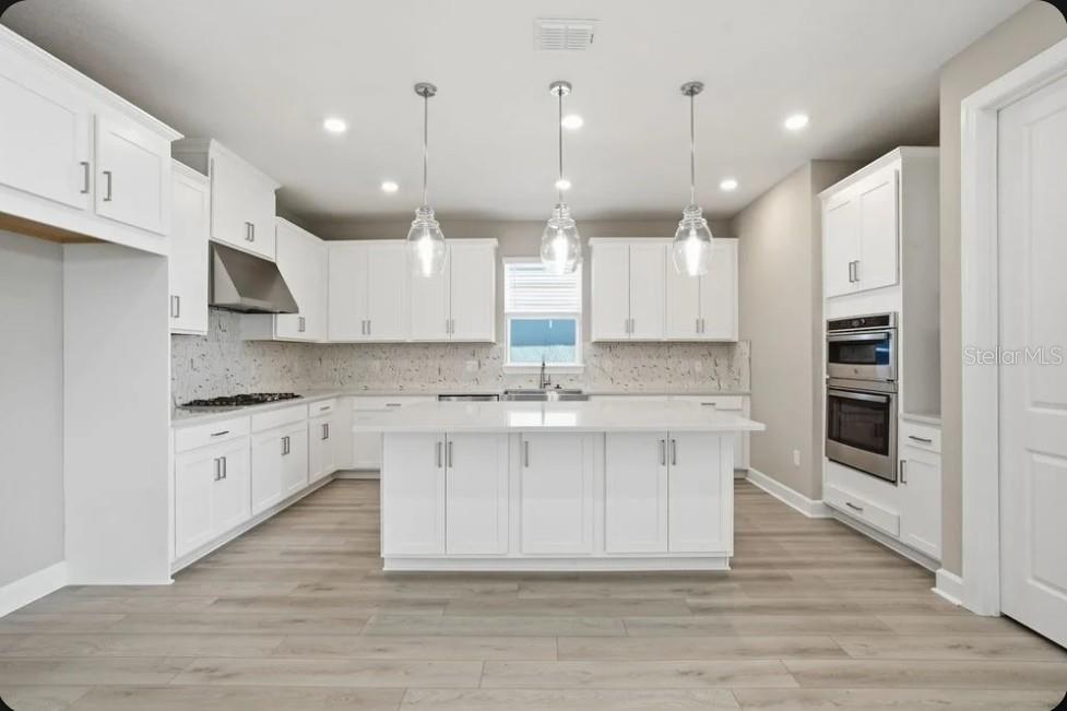 A modern kitchen features white cabinetry, a central island, stainless steel appliances, and light wood flooring — 7824 CASPIAN STREET, PALMETTO, FL