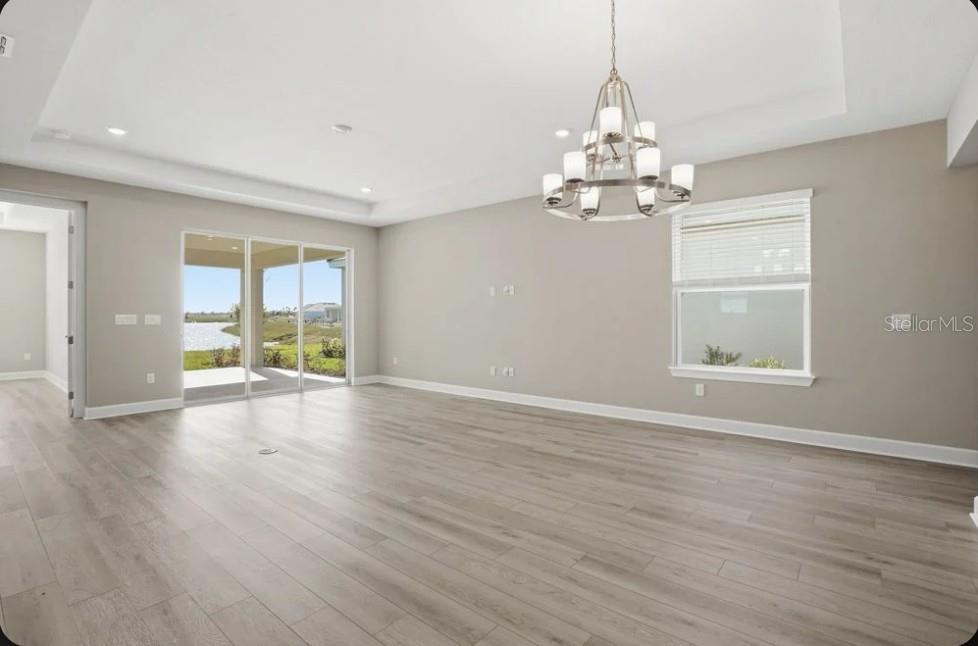 A spacious living room with light wood flooring, a chandelier, and sliding doors to a patio — 7824 CASPIAN STREET, PALMETTO, FL