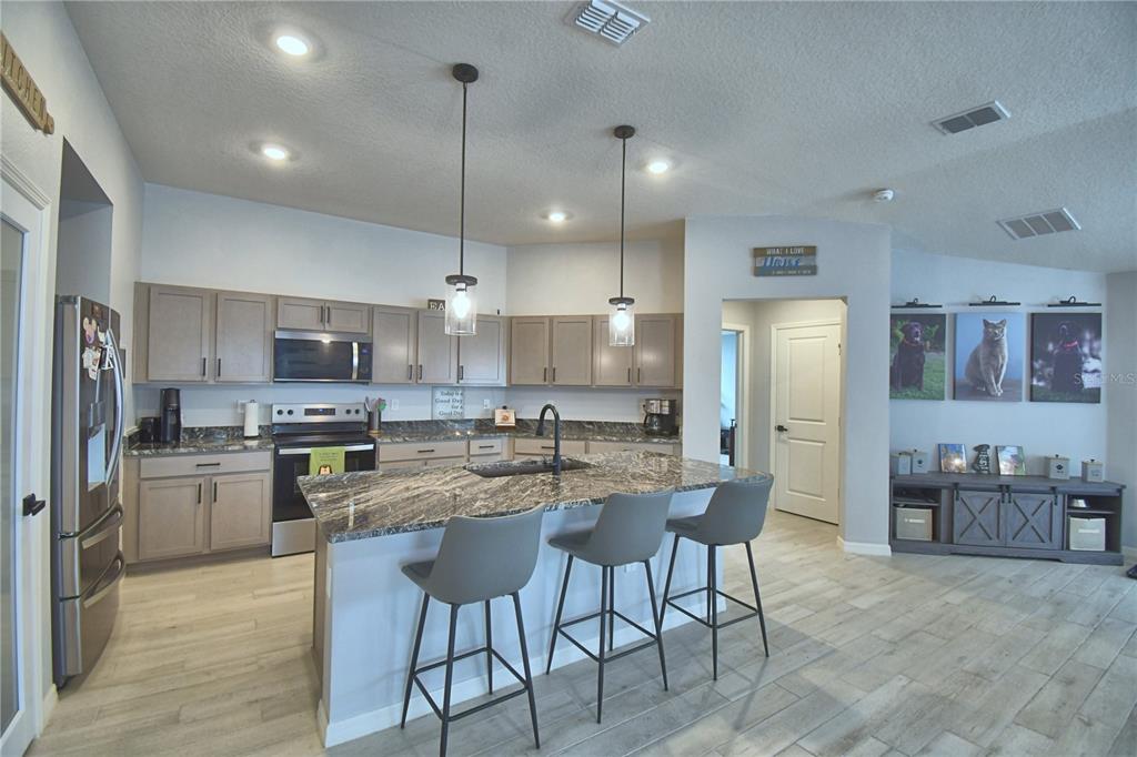 A kitchen with gray cabinets, a granite-topped island, and three bar stools on wood-look flooring — 2817 WOODACRE DRIVE, HAINES CITY, FL