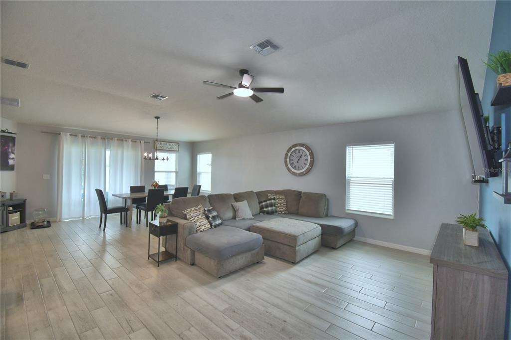 An open-concept living and dining area features light wood-look tile flooring and a sectional sofa — 2817 WOODACRE DRIVE, HAINES CITY, FL
