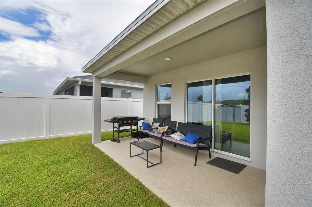 A covered concrete patio features a grill, outdoor seating, and a view of the backyard — 2817 WOODACRE DRIVE, HAINES CITY, FL