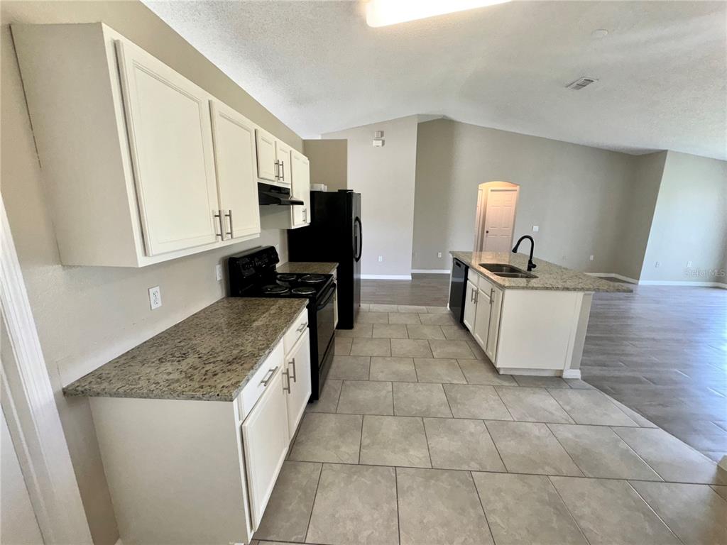 A kitchen features white cabinets, granite countertops, black appliances, and light-colored tile flooring — 1011 MORVAN LANE, KISSIMMEE, FL