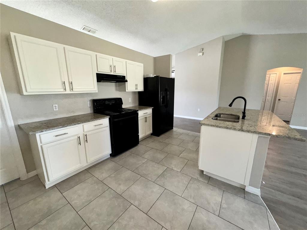 A kitchen features white cabinets, granite countertops, black appliances, and light-colored tile flooring — 1011 MORVAN LANE, KISSIMMEE, FL