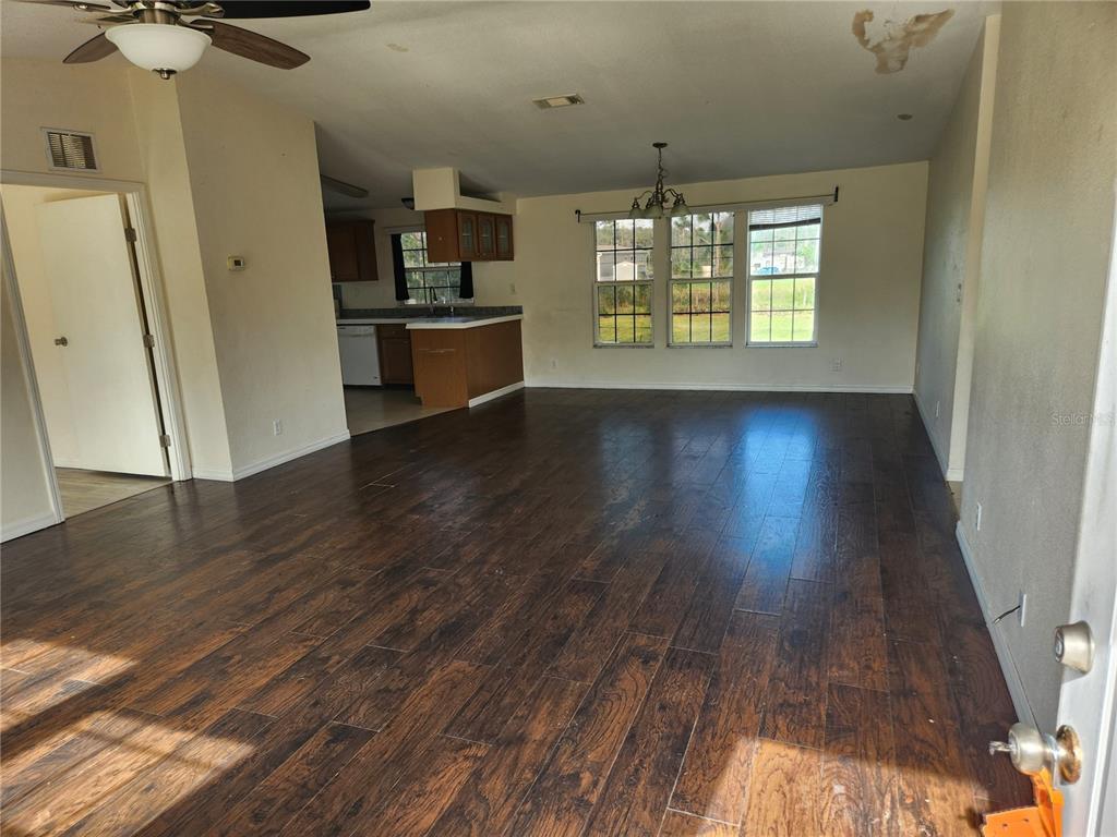 A living room with dark wood-look flooring, a ceiling fan, and an adjacent kitchen area — 5165 TOPEKA AVENUE, ST CLOUD, FL