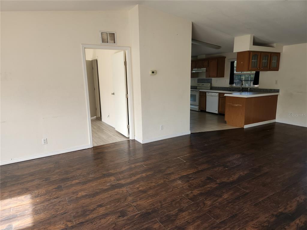 A living room with dark wood-look flooring leads to a kitchen with wooden cabinets — 5165 TOPEKA AVENUE, ST CLOUD, FL