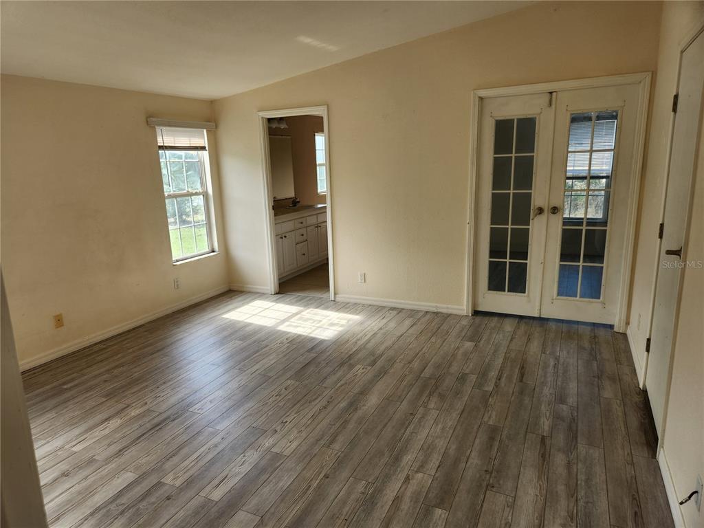 A bedroom with light-colored walls, wood-look flooring, a window, a bathroom doorway, and French doors — 5165 TOPEKA AVENUE, ST CLOUD, FL
