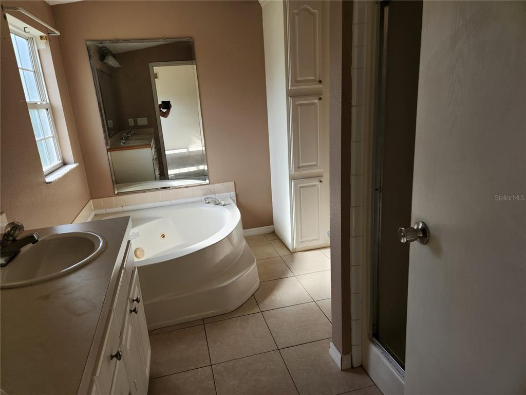 A bathroom features a corner jetted tub, a vanity with a sink, and tile flooring — 5165 TOPEKA AVENUE, ST CLOUD, FL