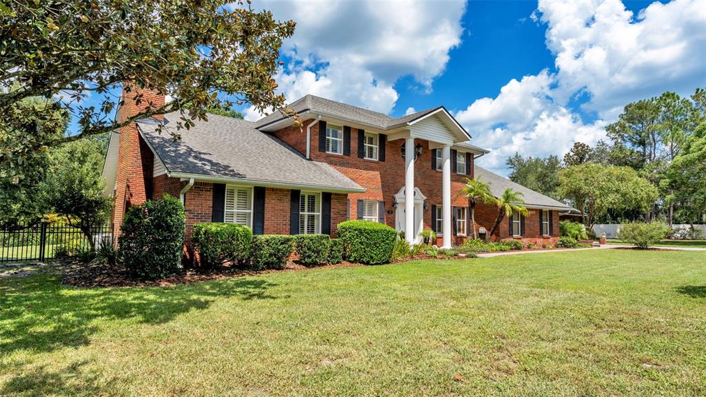 A two-story brick house with a columned portico sits on a large grassy lawn — 6605 POLEY CREEK DRIVE W, LAKELAND, FL
