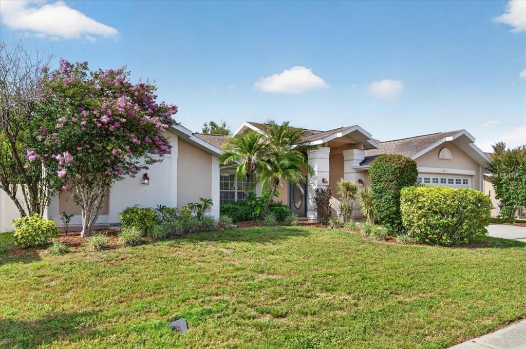 A single-story house with a tan exterior, a front lawn, and a flowering tree — 854 CHRISTINA CIRCLE, OLDSMAR, FL