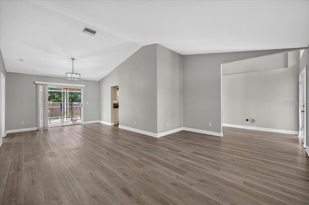 An empty living room features gray walls, wood-look flooring, a vaulted ceiling, and sliding glass doors — 854 CHRISTINA CIRCLE, OLDSMAR, FL