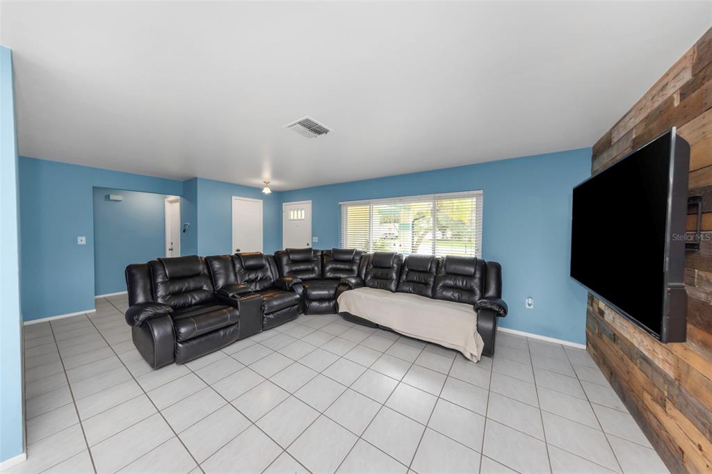 A living room features light blue walls, a large black sectional sofa, and wood-paneled wall accents — 9237 AMAZON DRIVE, NEW PORT RICHEY, FL