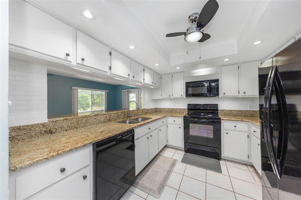 A kitchen features white cabinets, granite countertops, black appliances, and a ceiling fan — 9237 AMAZON DRIVE, NEW PORT RICHEY, FL