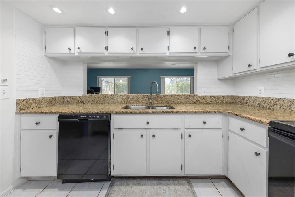 A kitchen features white cabinets, granite countertops, a black dishwasher, and a pass-through window — 9237 AMAZON DRIVE, NEW PORT RICHEY, FL