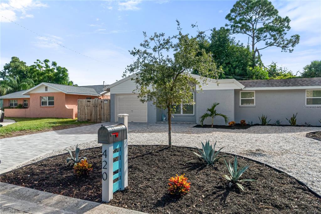 A gray single-story house with a paved driveway, gravel yard, and a modern mailbox post — 420 MELODY CIRCLE, SARASOTA, FL
