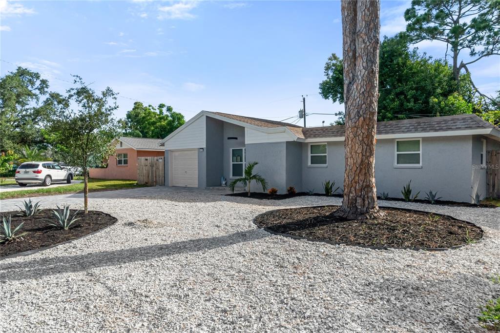 A single-story house with a gravel driveway, a large pine tree, and gray exterior siding — 420 MELODY CIRCLE, SARASOTA, FL