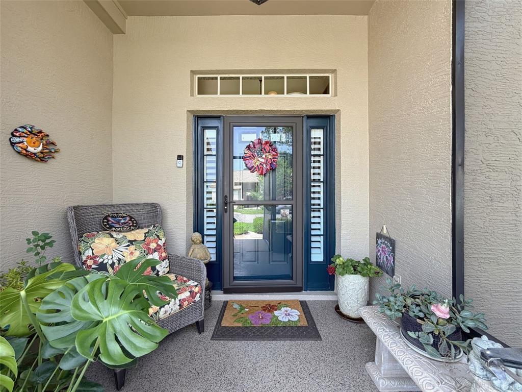 A covered entryway features a front door with sidelights, a wicker chair, and potted plants — 18412 BENT PINE DRIVE, HUDSON, FL
