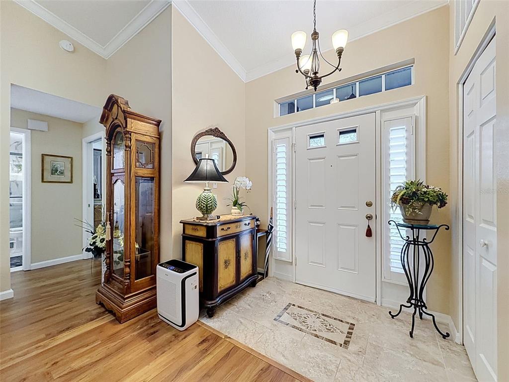 A foyer features a tile floor transition to wood, a grandfather clock, and a front door — 18412 BENT PINE DRIVE, HUDSON, FL