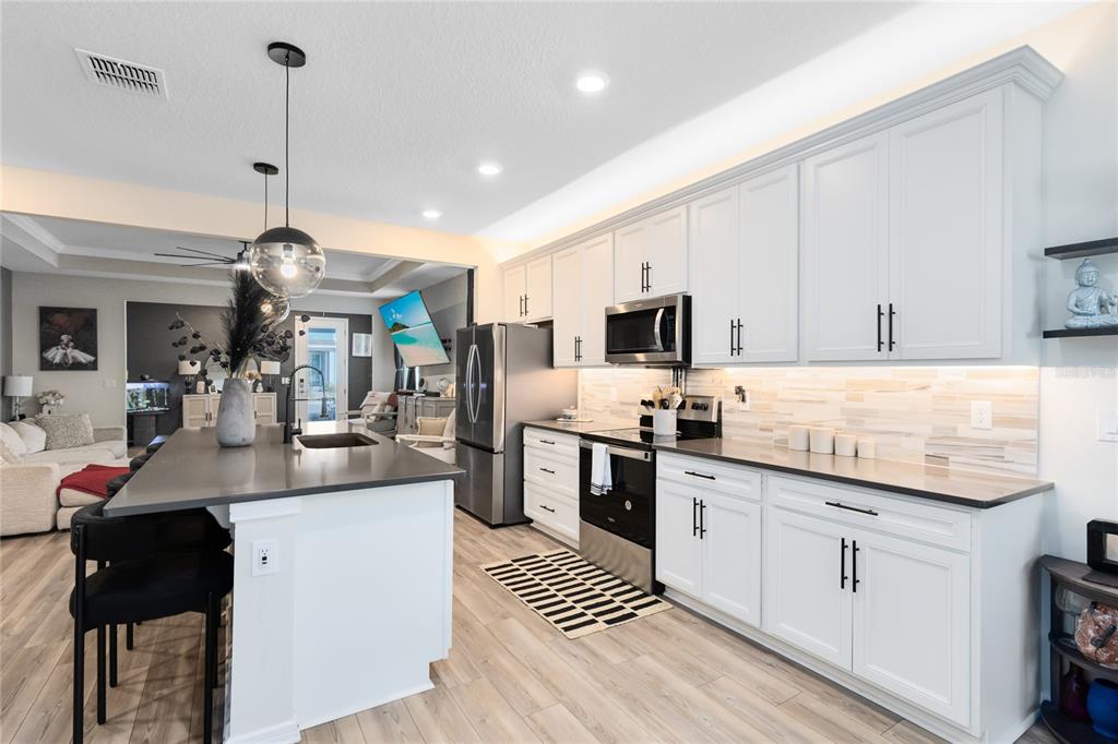 A modern kitchen features white cabinetry, stainless steel appliances, a gray island, and wood-look flooring — 6528 ROVER WAY, ST CLOUD, FL