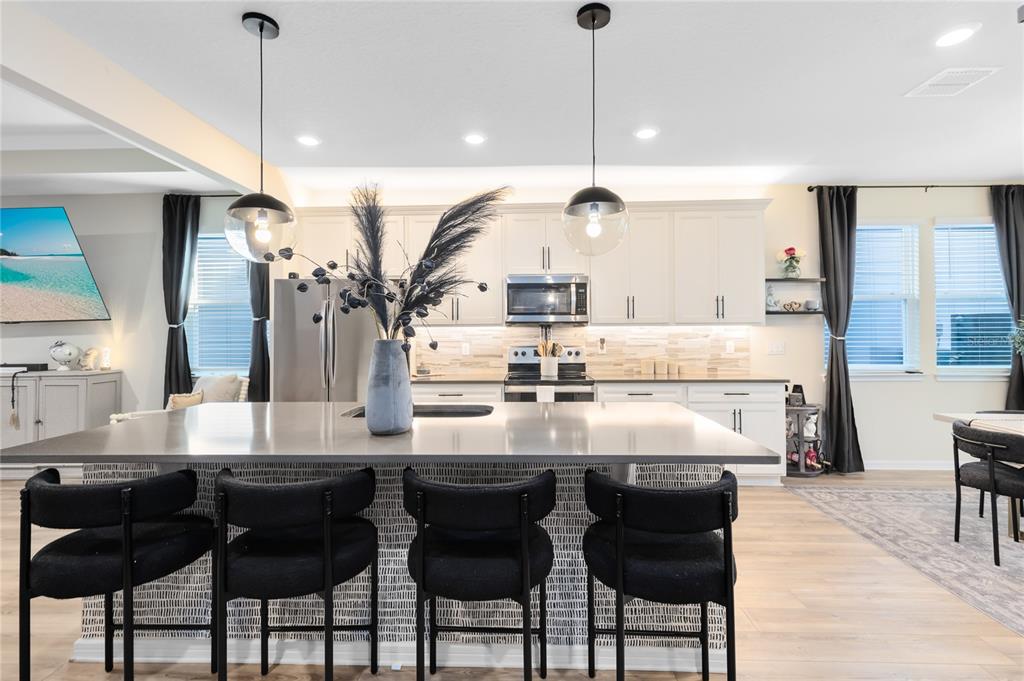 A kitchen features a large island with black bar stools and white cabinetry — 6528 ROVER WAY, ST CLOUD, FL