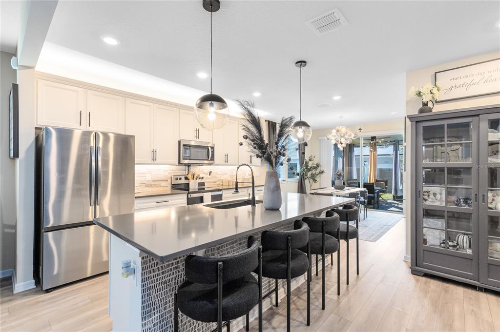 A modern kitchen features a large island with bar seating, white cabinetry, and stainless appliances — 6528 ROVER WAY, ST CLOUD, FL