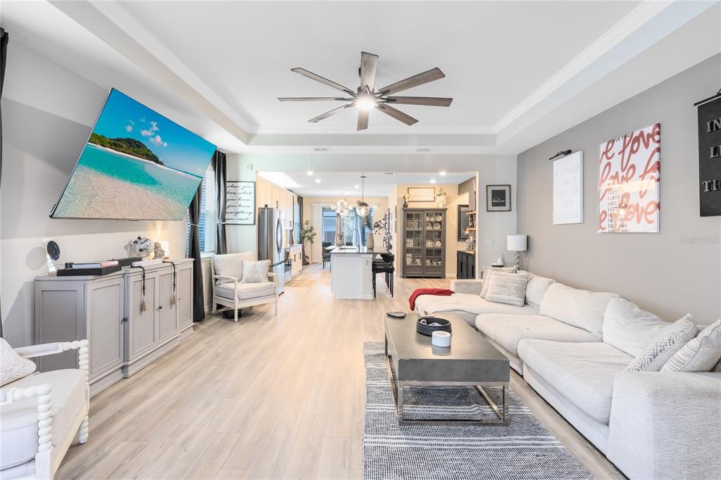 An open-concept living room features light wood flooring, a large sectional sofa, and a television — 6528 ROVER WAY, ST CLOUD, FL