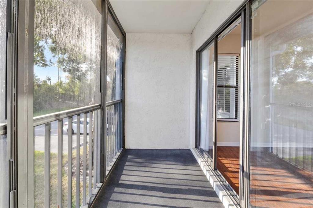 This virtually staged living room features a blue sofa, patterned armchairs, and a sliding glass door — 1127 PINE RIDGE CIRCLE W UNIT A2, TARPON SPRINGS, FL