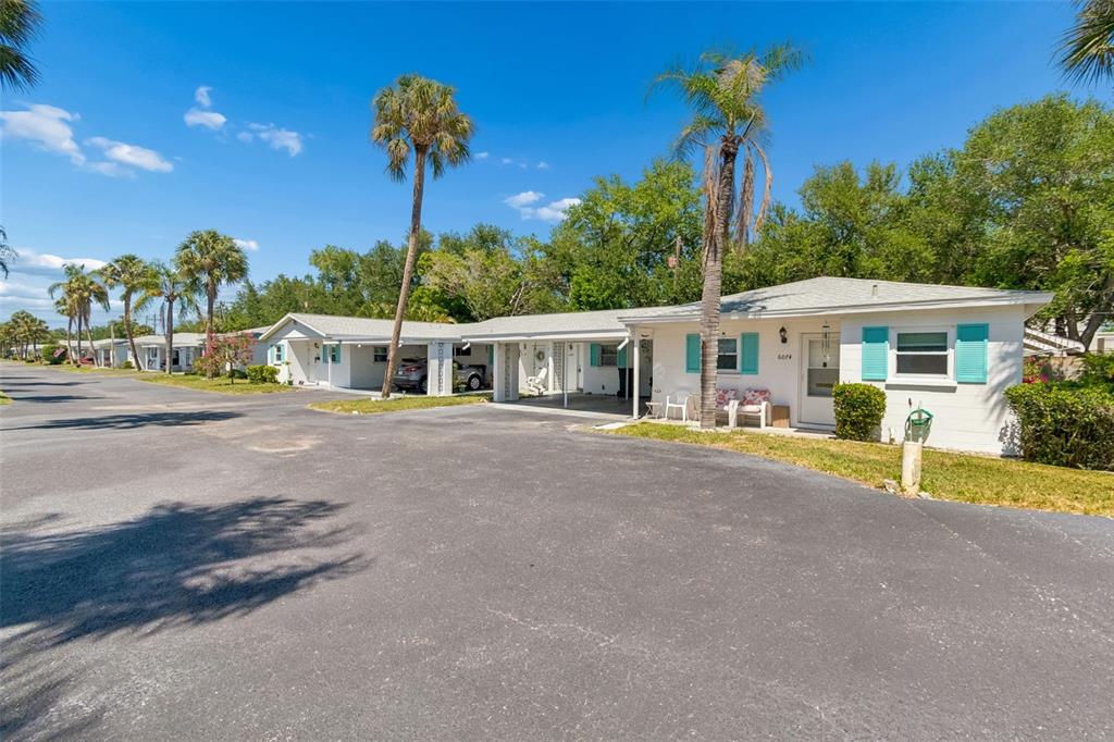 A row of single-story white houses with turquoise shutters and carports along a paved street — 6072 ARLENE WAY, BRADENTON, FL