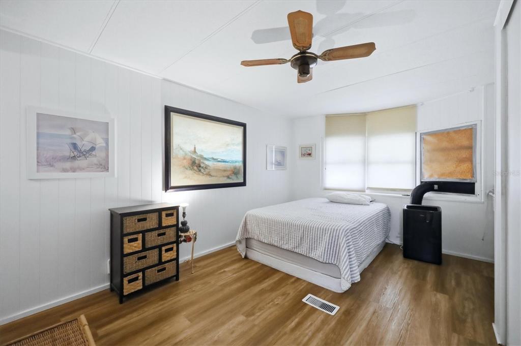 A bedroom features white paneled walls, wood-look flooring, a ceiling fan, and a portable air conditioner — 4917 1ST A STREET E, BRADENTON, FL