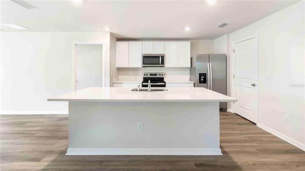 A modern kitchen features white cabinetry, stainless steel appliances, and a large central island — 10931 RABBIT GROVE TRAIL, PARRISH, FL