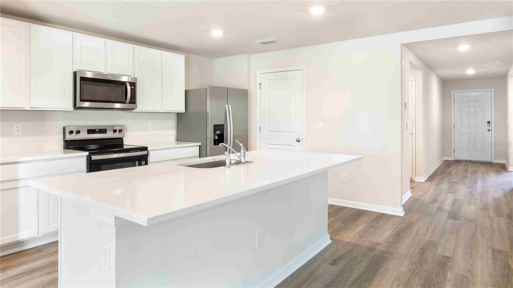 A modern kitchen features white cabinets, stainless steel appliances, and a large white quartz island — 10931 RABBIT GROVE TRAIL, PARRISH, FL