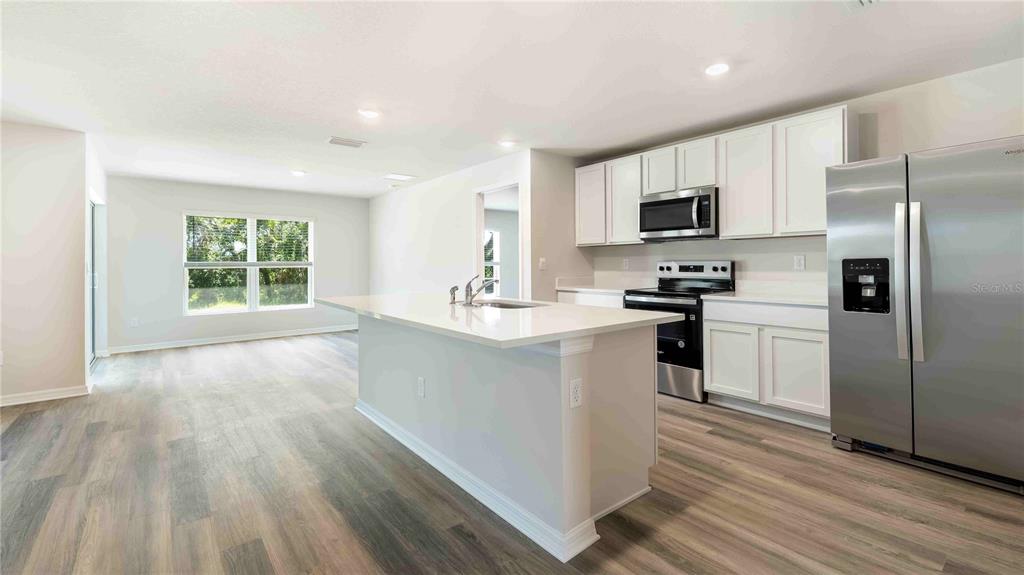 A modern kitchen features white cabinets, stainless steel appliances, and a large central island — 10931 RABBIT GROVE TRAIL, PARRISH, FL