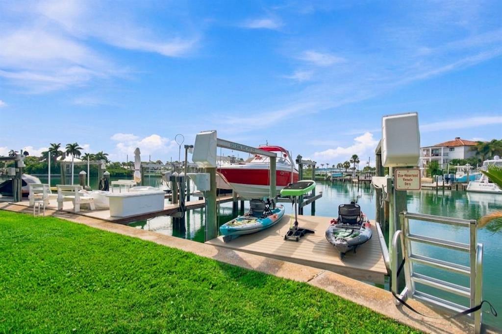 A paved patio with outdoor seating overlooks a grassy lawn, boat docks, and a waterway — 245 116TH AVENUE UNIT 245, TREASURE ISLAND, FL