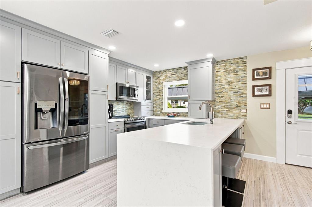 A modern kitchen features gray cabinets, stainless steel appliances, a white island, and tiled backsplash — 245 116TH AVENUE UNIT 245, TREASURE ISLAND, FL