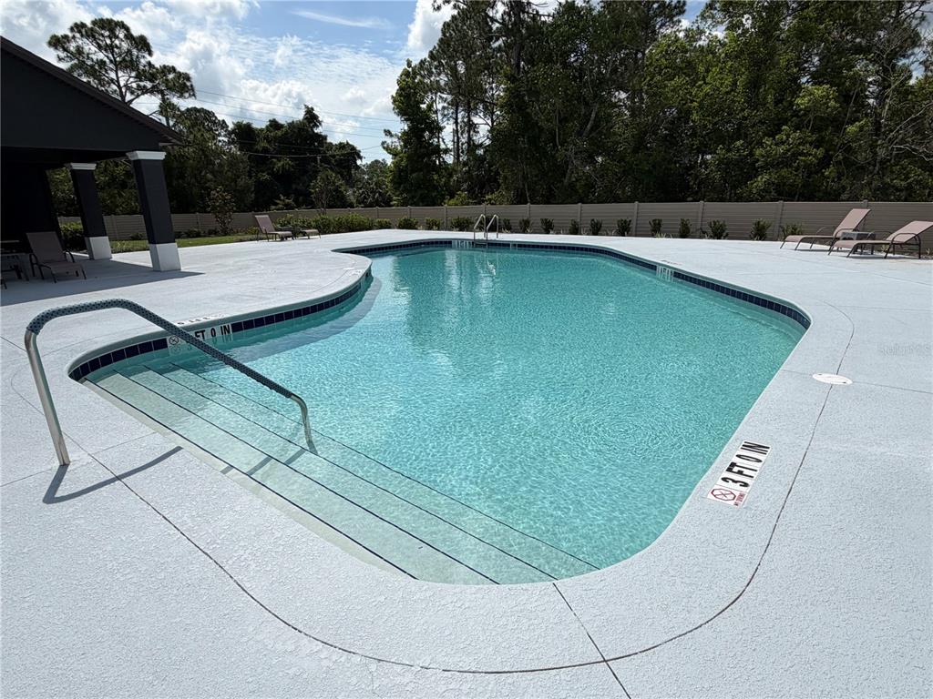 An outdoor swimming pool with a shallow entry area, metal handrails, and surrounding lounge chairs — 34 GREEN CIRCLE UNIT 101, PALM COAST, FL