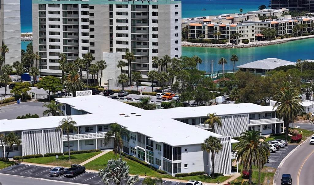 An aerial view shows a white multi-story apartment building with a flat roof and parking — 7050 SUNSET WAY UNIT 19, ST PETE BEACH, FL