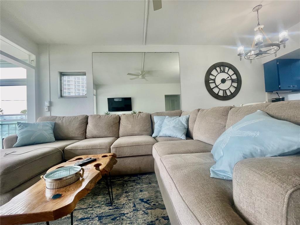 A living room features a large beige sectional sofa, a live-edge coffee table, and a mirror — 7050 SUNSET WAY UNIT 19, ST PETE BEACH, FL