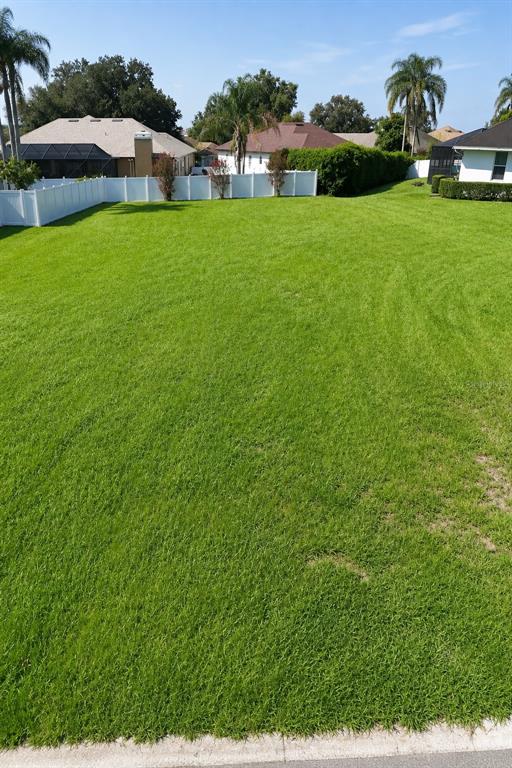 A large, vacant residential lot covered in green grass with a white vinyl fence — 2116 LONGLEAF CIRCLE, LAKELAND, FL
