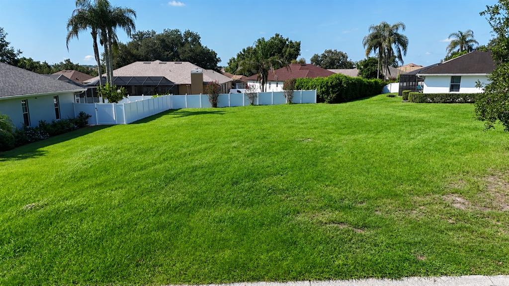 A large, grassy backyard is enclosed by a white vinyl fence with neighboring houses nearby — 2116 LONGLEAF CIRCLE, LAKELAND, FL