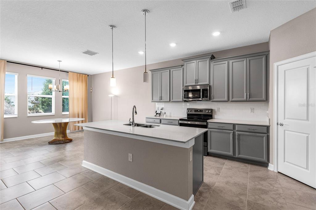 A kitchen features gray cabinets, a central island with a sink, and a dining area — 8833 BETH PAGE LN, DAVENPORT, FL