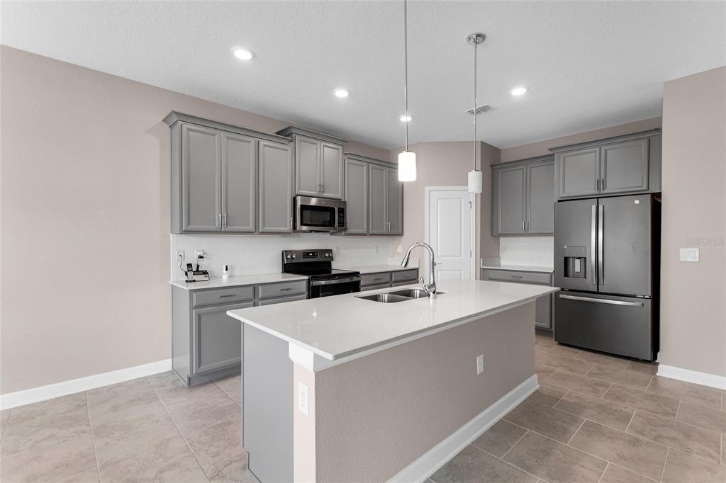 A modern kitchen features gray cabinets, white countertops, a central island, and stainless steel appliances — 8833 BETH PAGE LN, DAVENPORT, FL