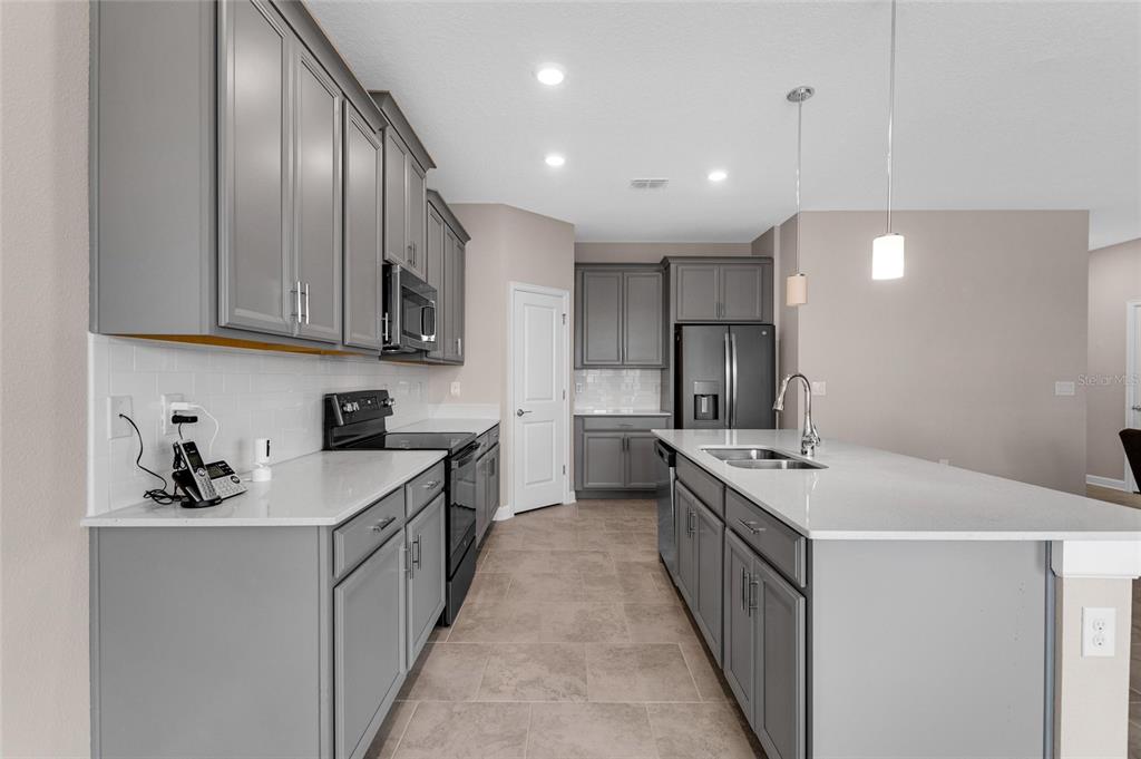 A kitchen features gray cabinets, white countertops, a center island, and stainless steel appliances — 8833 BETH PAGE LN, DAVENPORT, FL