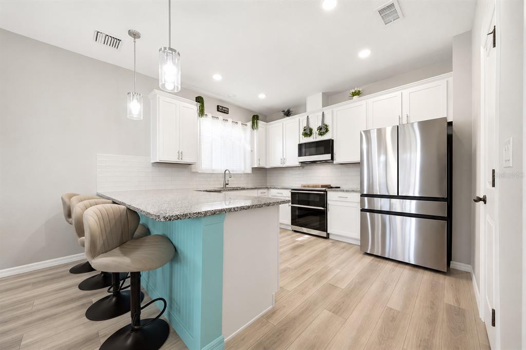 A kitchen features white cabinets, granite countertops, a turquoise island, and stainless steel appliances — 11520 GALLATIN TRAIL, PARRISH, FL