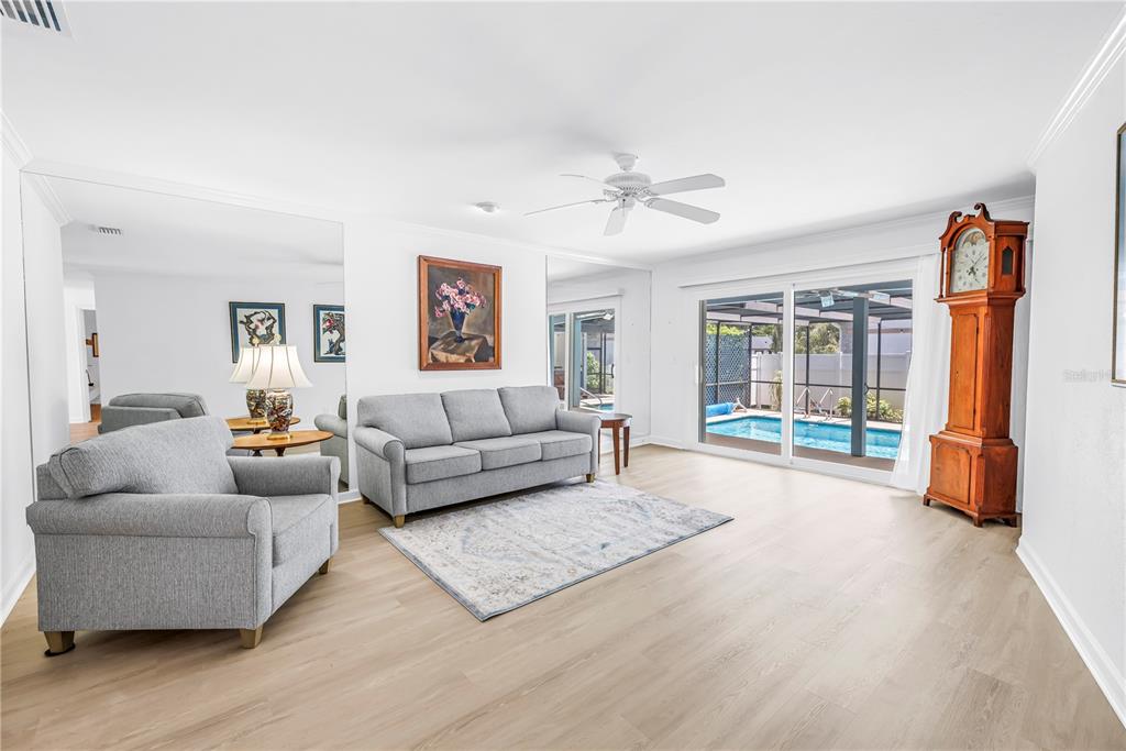 A living room with light wood floors, a grey sofa, an armchair, and a pool view — 3000 HERON PLACE, CLEARWATER, FL