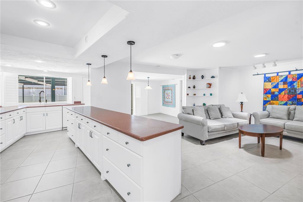 An open-concept kitchen with a large island and white cabinets overlooks a living room area — 3000 HERON PLACE, CLEARWATER, FL