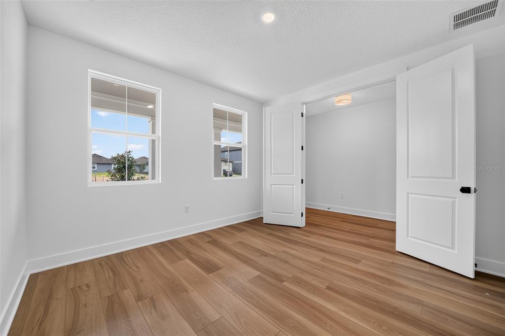 A room with light-colored walls, wood-look flooring, two windows, and open double doors — 30106 EMERALD FOREST DRIVE, MOUNT DORA, FL