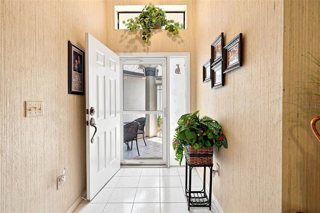 An entryway with tiled floors, textured wallpaper, a potted plant, and a white front door — 9239 TURNBERRY COURT, NEW PORT RICHEY, FL