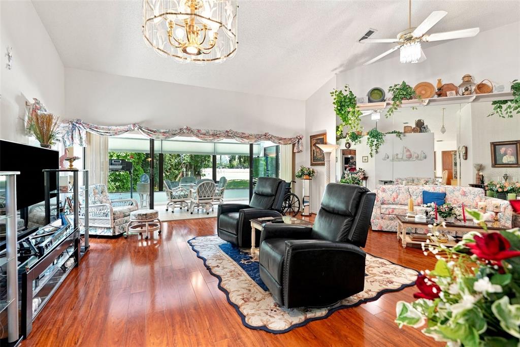 A living room with hardwood floors, two black leather recliners, and a view of a patio — 9239 TURNBERRY COURT, NEW PORT RICHEY, FL