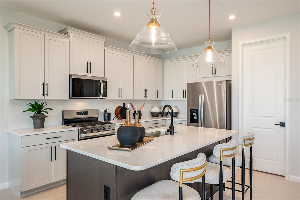 A modern kitchen features white cabinetry, a dark island with bar seating, and stainless steel appliances — 34897 FLOWER PATCH DRIVE, DADE CITY, FL