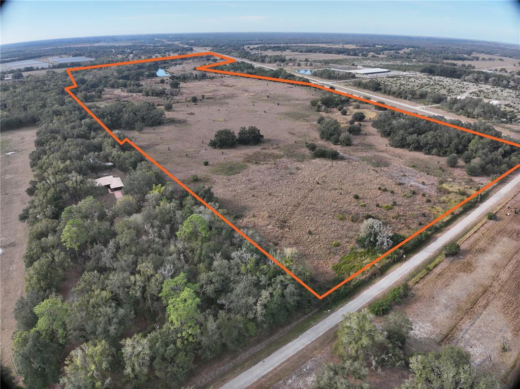 An aerial view shows a large, open grassy field outlined in orange with surrounding trees — 100AC NE HWY 17, ARCADIA, FL